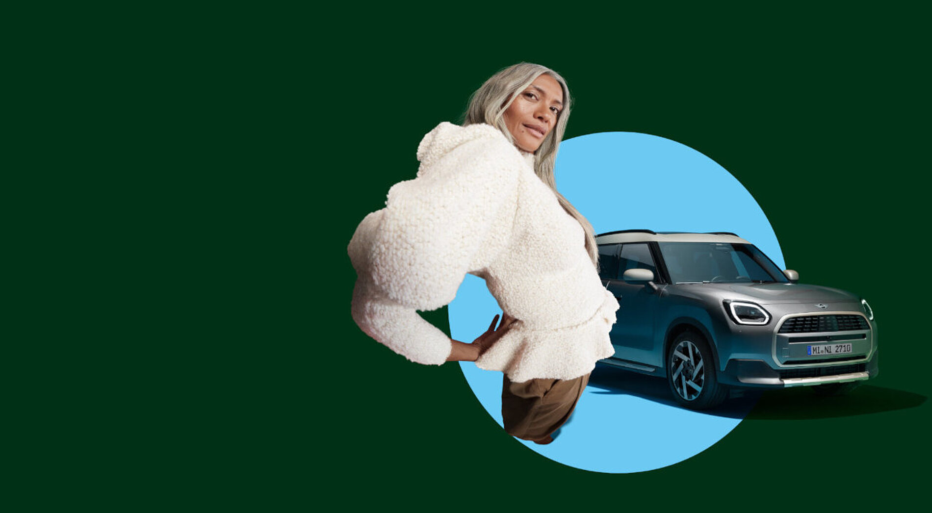 Ein weibliches Model mit weißer Wolljacke steht vor einem silbernen MINI Countryman.